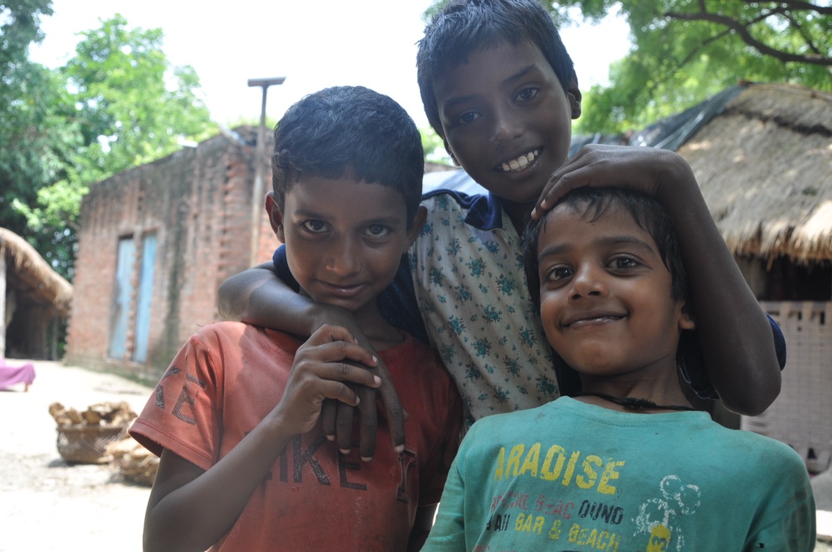 Three boys from Masauli village with their arms around each other, smiling