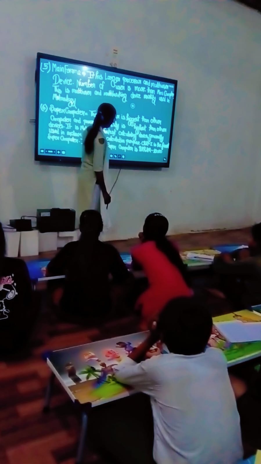 A student teaching a lesson on the interactive smartboard at Gajanand Learning Centre while classmates watch
